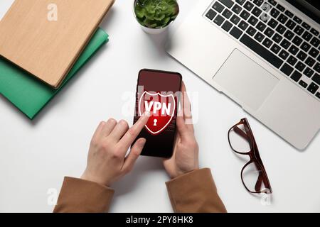 Frau, die ein Smartphone mit eingeschaltetem VPN am weißen Tisch verwendet, Draufsicht Stockfoto