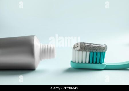 Bürste mit dunkelkohlensäurehaltiger Zahnpasta und Tube auf hellem Hintergrund, Nahaufnahme Stockfoto