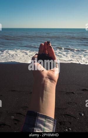 Nahaufnahme Frau hält einen Haufen schwarzen Sand auf dem Konzeptfoto des Strandes Stockfoto