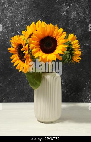 Vase mit wunderschönen Sonnenblumen auf weißem Tisch vor schwarzem Hintergrund Stockfoto