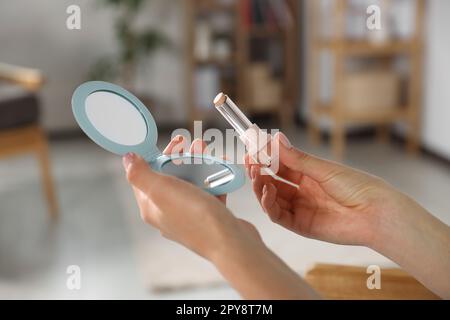 Junge Frau mit Kosmetikspiegel und Lippenstift im Haus, Nahaufnahme Stockfoto