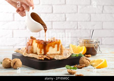 Frau, die Karamellsauce auf köstliche Käsekuchen am Holztisch gießt, Nahaufnahme Stockfoto