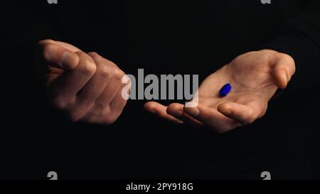Studiofoto männliche Hände zeigen blaue Pille isoliert auf schwarzem Hintergrund. Konzept der richtigen Wahl. Stockfoto