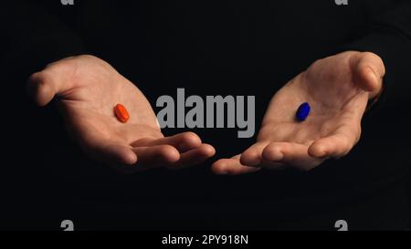 Studiofoto männliche Hände zeigen rote Pille und blaue Pille isoliert auf schwarzem Hintergrund. Konzept der richtigen Wahl. Stockfoto