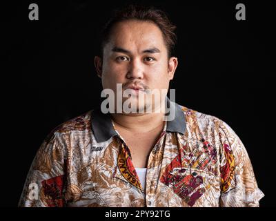 Porträt eines asiatischen Mannes, das vor einem horizontalen Bild mit schwarzem Hintergrund in die Kamera schaut Stockfoto