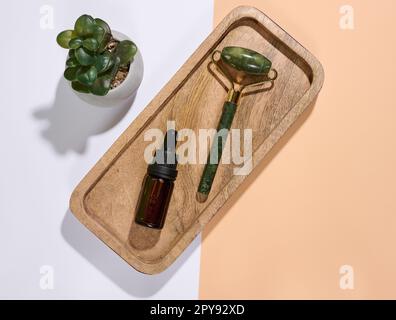 Handmassagegerät für das Gesicht und braune Glasflasche mit Tropfen auf Marmorplatte, Draufsicht Stockfoto