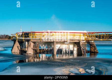 Eisbedeckte Metallkonstruktion eines Auslaufrohrs an einem kleinen Staudamm Stockfoto