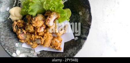 Tako Karaage (frittierter Tintenfisch), japanische Meeresfrüchte auf schwarzem Keramikteller mit Salat, Zitrone und Mayonnaise. Draufsicht Stockfoto