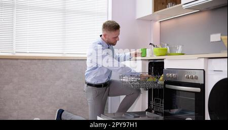 Junger Mann, Der Trinkglas Aus Der Spülmaschine Nimmt Stockfoto