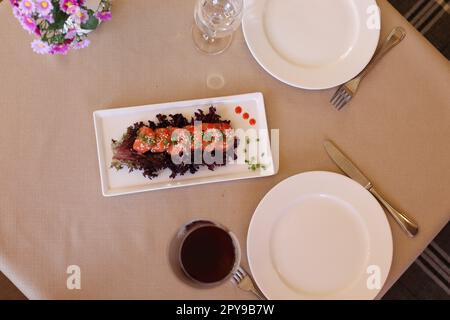 Ein Blick von oben auf Garnelen mit Sesam und Gemüse, serviert auf einem weißen Tablett neben einem Glas Wein und leeren Tellern Stockfoto