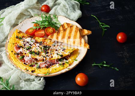 Gebratenes Omelette gefüllt mit Wurst, Tomaten, Gemüse und Käse. Leckeres, einfaches Frühstück Stockfoto