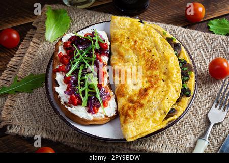 Gebratenes Omelett gefüllt mit Pilzen und Sandwich mit gegrillten Paprika und karamellisierten Zwiebeln Stockfoto