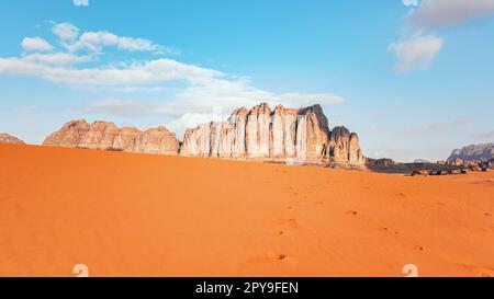 Orange Sandwüste, felsige Felsformationen und Berghintergrund, blauer Himmel darüber, Camp Zelte aus der Ferne sichtbar - typische Landschaft in Wadi Rum, Jordanien Stockfoto