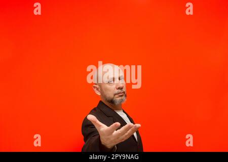 Porträt eines stilvollen Geschäftsmannes, der Handgesten macht. Ich schaue in die Kamera. Isoliert auf orangefarbenem Hintergrund. Stockfoto