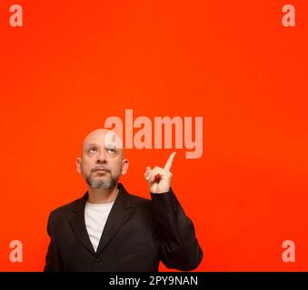 Geschäftsmann, erwachsen, elegant, zeigt mit dem Finger nach oben. Isoliert auf orangefarbenem Hintergrund. Stockfoto