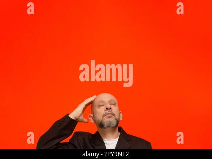 Geschäftsmann, trägt eine schwarze Anzugjacke, schlau und aufmerksam. Isoliert auf orangefarbenem Hintergrund. Stockfoto