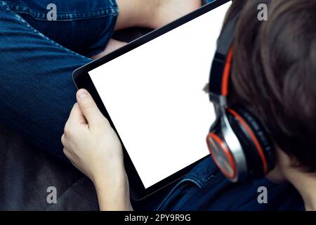 Digitaler Tablet-Computer mit leerem weißen Bildschirm in männlichen Händen, Nahaufnahme von oben. Junger Typ mit Kopfhörern. Stockfoto