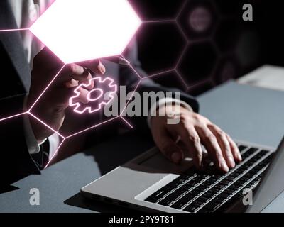 Mann im Büroanzug sitzt am Tisch mit Laptop und tippt Text. Geschäftsmann hält Stift und drückt virtuellen Knopf. Futuristisches Styling mit farbigem Schein. Stockfoto