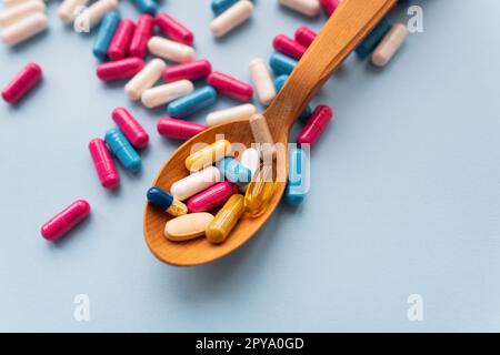 Verschiedene helle Pillen auf blauem Hintergrund liegen in einem Holzlöffel vor dem Hintergrund verschiedener heller Pillen. Gesundheitskonzept, Nahaufnahme. Stockfoto