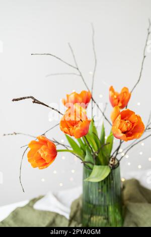 Ein sehr schöner Frühlingsstrauß in einer grünen Vase steht auf einem Tisch auf einer Tischdecke aus Leinen, orangefarbene Pfingstrosen. Stockfoto