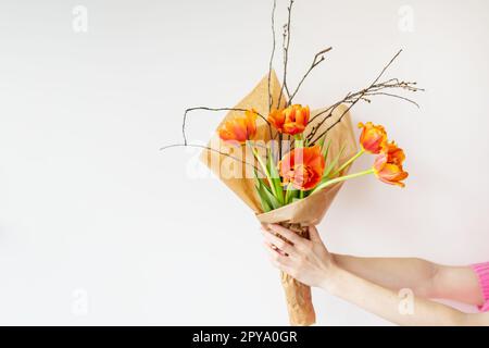 Das Mädchen hält in ihren Händen einen sehr schönen Frühlingsstrauß aus orangefarbenen Pfingstropfen zusammen mit Zweigen junger Kirschen. Stockfoto