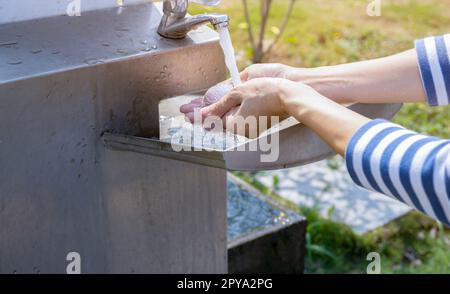 World Water Day Konzept. Frau wäscht sich die Hände mit Leitungswasser unter fließendem Wasserhahn am Edelstahlwaschbecken. Hände mit Leitungswasser am Waschbecken im Freien waschen. Persönliche Hygiene. Wasserverbrauch und Nachhaltigkeit. Stockfoto