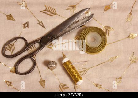 Rolle mit goldenem Gewinde und Schere mit Kaugummi auf metallischem Stoff Stockfoto