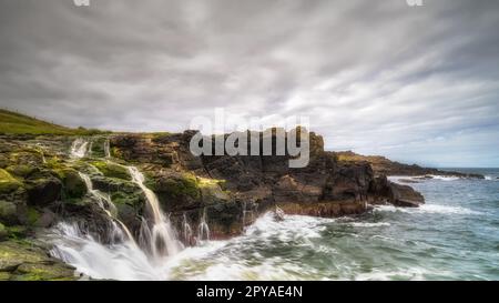 Dunseverick Falls mit kleinen Klippen und Wasserstreifen, die hinunter in den Atlantischen Ozean, Nordirland, fallen Stockfoto