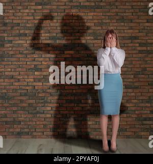 Geschäftsfrau und Schatten einer starken, muskulösen Dame hinter ihr auf einer Ziegelwand. Konzept der inneren Festigkeit Stockfoto