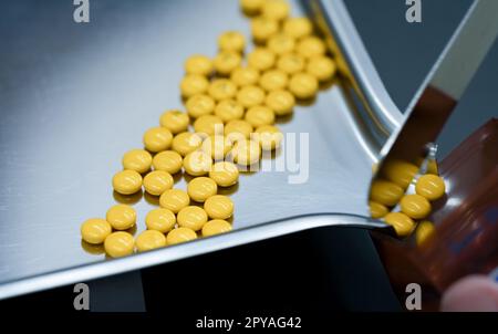 Selektiver Fokus auf gelbe Tabletten Pillen auf rostfreiem Tablett mit verschwommener Hand des Apothekers oder Apothekentechnikers, die Pillen in einen Plastikbeutel mit Reißverschluss zählen. Verschreibungspflichtige Medikamente. Medizinische Versorgung. Stockfoto