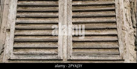 Alte Holzläden am Fenster. Antike Holzarchitektur. Trockenes Holz mit rostender, verfärbter Farbe. Schalen und Staub. Natürliche Farbe. Fensterbank, horizontale Streifen und Leisten. Stockfoto