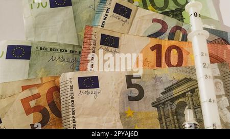 Euro-Papiernoten. Europäische Währung auf weißem Hintergrund. Eine Dosierspritze neben Geld. Die hohen Behandlungskosten. Scheine für 5, 10, 20, 50 und 100 Euro Stockfoto