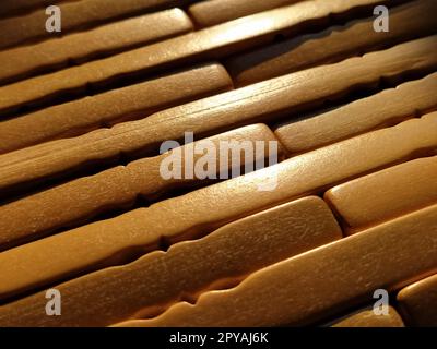 schilf- oder Holzmatte. Der Teppich ist eine Matte unter dem heißen Wasser. Gestrickte Holzstäbe mit abgerundeten Kanten. Nahaufnahme. Gelb, Braun und Beige. Seitenbeleuchtung. Traditionelle Bambuspolsterung Stockfoto