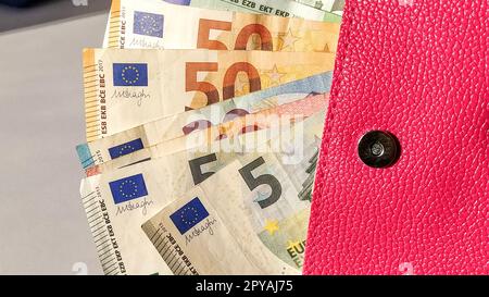 Euro-Papiernoten. Europäische Währung auf weißem Hintergrund. Eine Handtasche oder Handtasche in leuchtendem Rosa mit einem Metallknopf, aus der das Geld in einem Fächer verteilt wird. Banknoten von 5, 10, 20, 50 und 100 Stockfoto