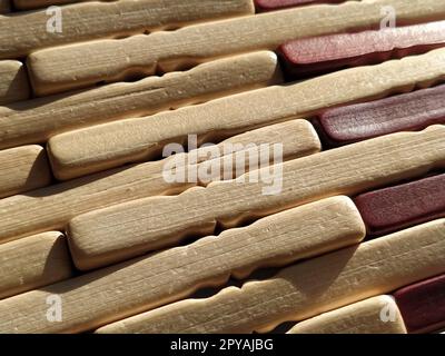 schilf- oder Holzmatte. Der Teppich ist eine Matte unter dem heißen Wasser. Gestrickte Holzstäbe mit abgerundeten Kanten. Nahaufnahme. Gelb, Braun und Beige. Seitenbeleuchtung. Traditionelle Bambuspolsterung Stockfoto