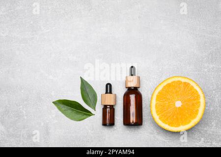 Flaschen mit ätherischem Öl mit orangefarbener Scheibe und Blättern auf grauem Tisch, flach liegend Stockfoto