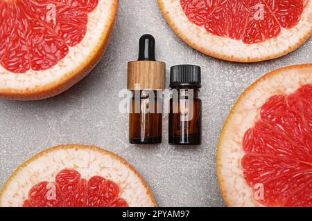 Flaschen ätherisches Öl mit Grapefruitscheiben auf grauem Tisch, flach liegend Stockfoto