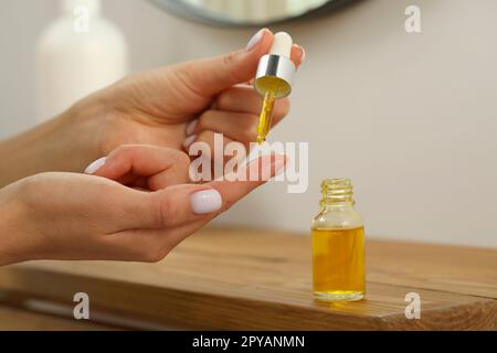 Junge Frau tropft ätherisches Öl auf den Finger im Haus, Nahaufnahme Stockfoto