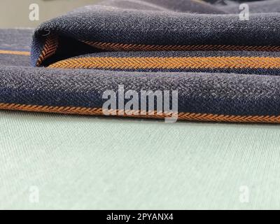 Grau-schwarzer Stoff mit orangefarbenen und blauen Streifen. Textilgewebe, das sauber auf der Oberfläche gefaltet ist. Naturwolle zum Nähen von Kleidung und Polstern. Lifestyle. Nahaufnahme. Weichzeichner Stockfoto