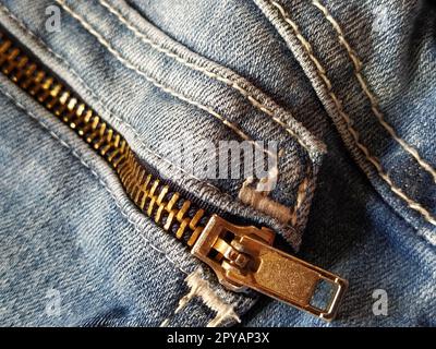 Denim-Material mit Nähten aus roten oder beigen Fäden. Textilstruktur. Reißverschluss aus rauem Metall. Aufgenähte Tasche. Blaue Farbe des Materials. Nähprodukt für die Leichtindustrie. Stockfoto