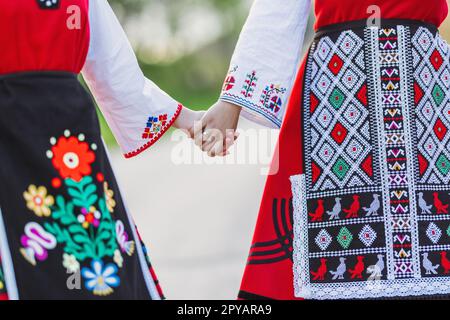 Mädchen in traditionellen bulgarischen ethnischen Kostümen mit folkloristischer Stickerei, die Händchen hält. Der Geist Bulgariens - Kultur, Geschichte und Traditionen. Stockfoto