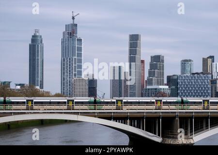 Züge überqueren die Grosvenor Railway Bridge in Battersea mit neuen hochaufragenden modernen Apartments in der Entwicklung mehrerer Gebäude in Nine Elms, die am 26. April 2023 in der Nähe von Vauxhall in London, Großbritannien, wachsen. Die Gegend um Vauxhall/Nine Elms wird stark umgestaltet und umgebaut, und es befinden sich riesige Hochhäuser im Bau. Zu den modernen Bauten der Gegend gehören stilvolle Apartmentgebäude aus Glas und Mauerwerk. Das Gebiet war früher industriell, aber es entwickelt sich jetzt zu Wohn- und Gewerbegebiet. Stockfoto