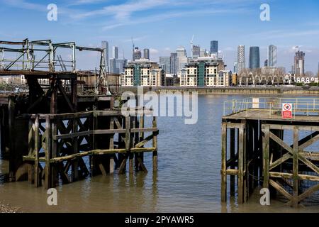 Verfallene und verrottete alte hölzerne Anlegestelle in Deptford mit dem Canary Wharf Finanzdistrikt in der Ferne gesehen am 29. April 2023 in London, Vereinigtes Königreich. Canary Wharf ist ein Gebiet in der Nähe der Isle of Dogs im Londoner Stadtteil Tower Hamlets und wird von der Greater London Authority als Teil des zentralen Londoner Geschäftsviertels definiert. Zusammen mit der City of London ist sie eines der wichtigsten Finanzzentren in Großbritannien und der Welt und beherbergt viele Hochhäuser, darunter das drittgrößte im Vereinigten Königreich, den One Canada Square. Stockfoto