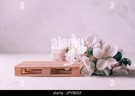 Holzpodium in Form einer Palette auf leichter Gipsfläche mit Apfelblumen. Sockel oder Tisch. Modell für Kosmetik Stockfoto