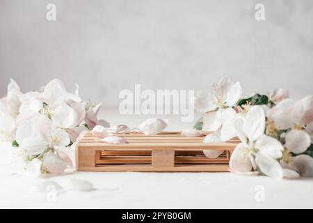 Holzpodium in Form einer Palette auf leichter Gipsfläche mit Apfelblumen. Sockel oder Tisch. Modell für Kosmetik Stockfoto