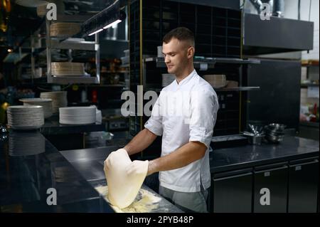 Koch wirft Teig in die Luft, während er Pizza zubereitet Stockfoto