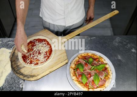 Über dem Blick auf die Hand des Küchenchefs beim Zubereiten der Pizza in einer professionellen Küche Stockfoto