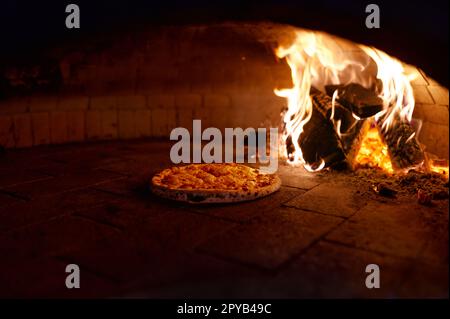 Pizza wird in einem traditionellen Holzofen mit offenem Kamin zubereitet Stockfoto