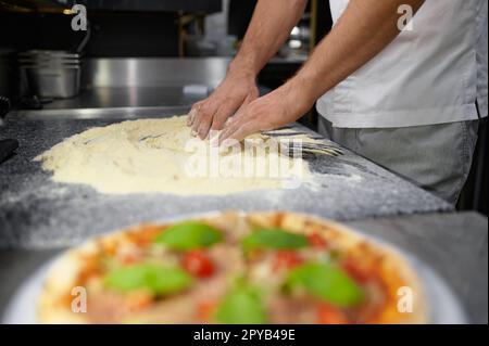 Der Küchenchef mischt Mehl, um Pizzateig zu kneten Stockfoto