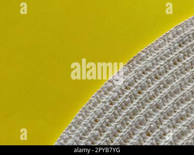 Strohhut auf gelbem Hintergrund. Der Rand des breiten Schirms des Hutes. Fäden oder Zweige binden. Nahaufnahme. Sommerferien-Thema Stockfoto